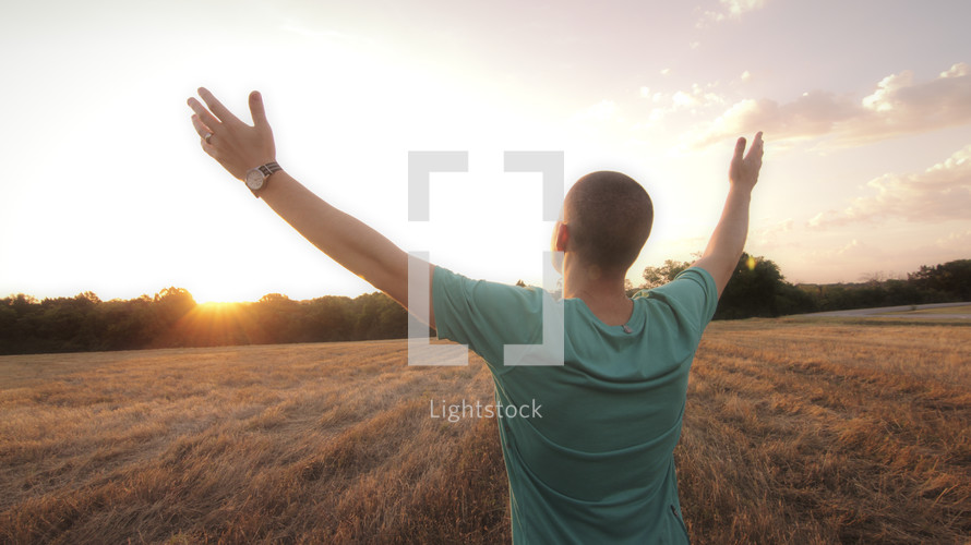 Man in field worshipping at sunrise