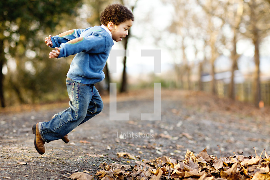 Boy jumping into leaves fall autumn road