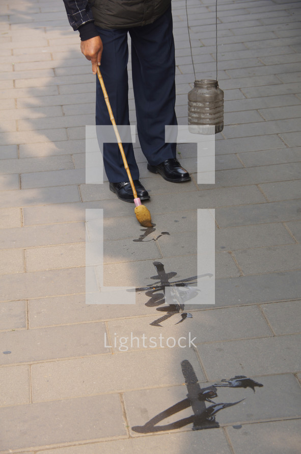 Old man painting Chinese symbols on a sidewalk with water