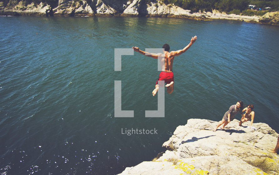 Male jumping off rock cliff into lake