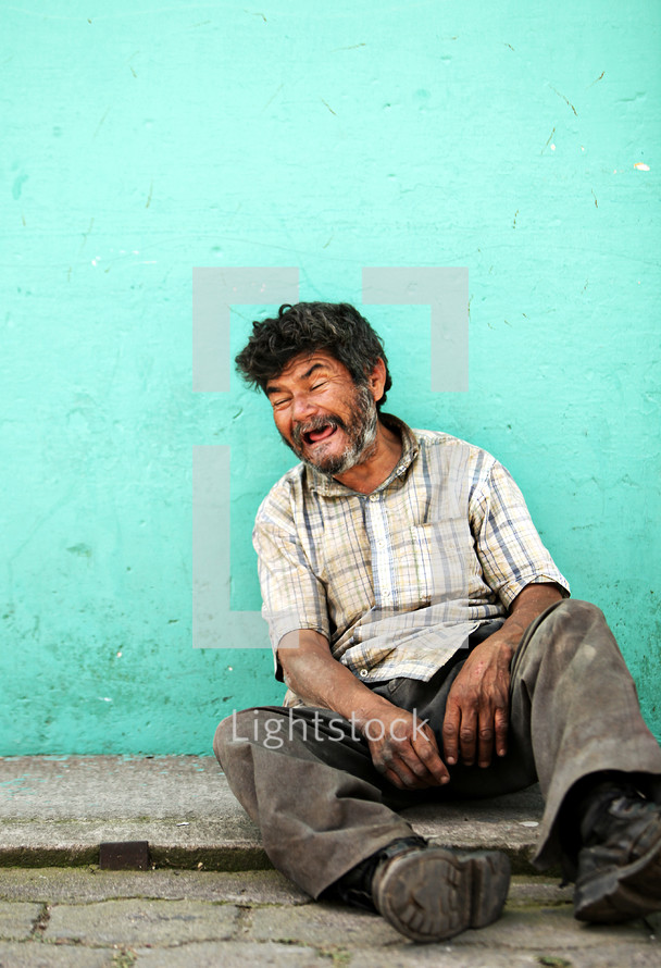 An elderly man sitting on a sidewalk 