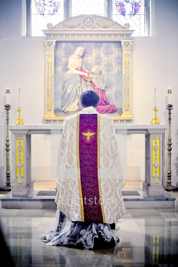 priest kneeling in prayer in front of an altar