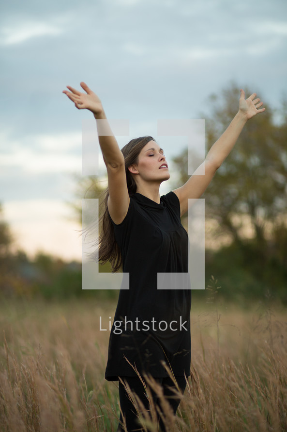 woman in a field with her hands raised in praise and worship to God