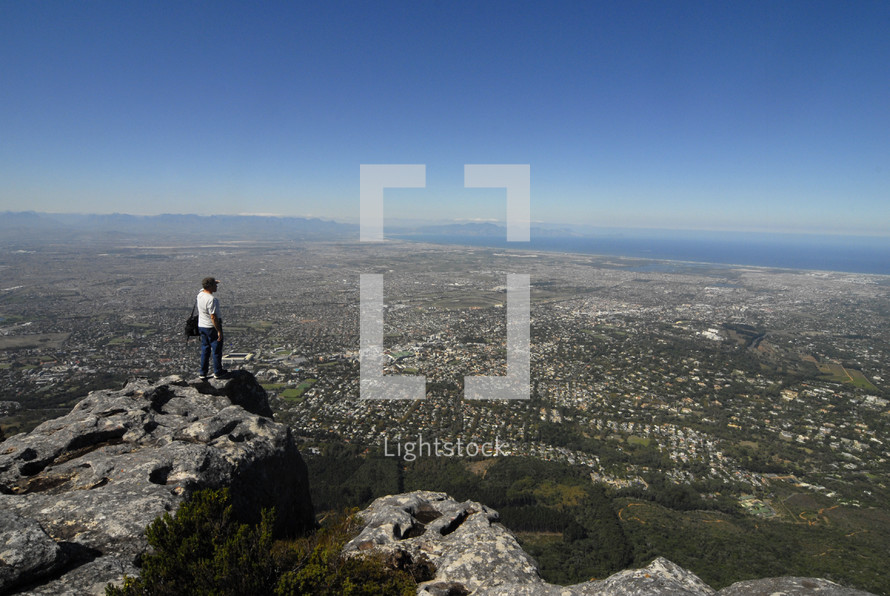 Man on mountain top looking out over a city by the sea