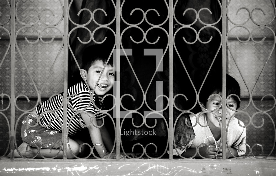 Two boys smile from a gated window