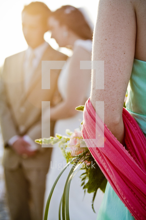 woman holding flowers with bride and groom in background