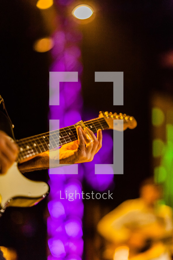 Hands playing electric guitar on lighted stage durning worship