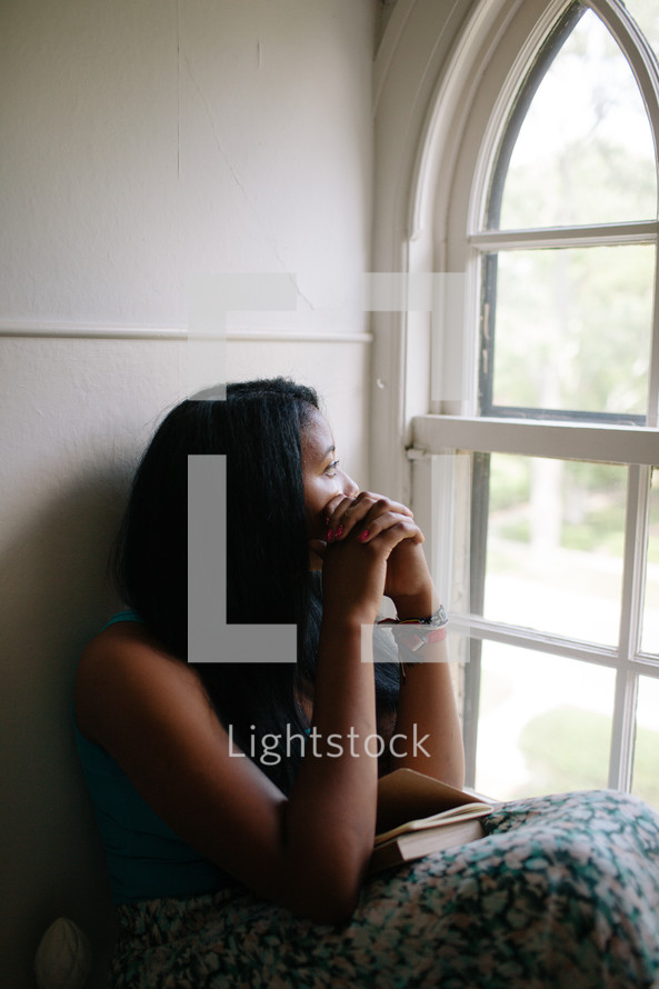 A woman looking out a pane glass window in prayer