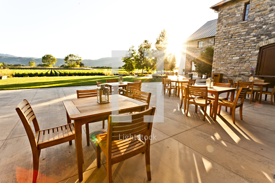 A patio with wood  tables and chairs at sunset over looking a vineyard napa valley