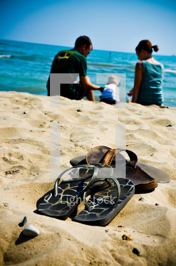 flip flops on a beach in front of a family playing in the sand