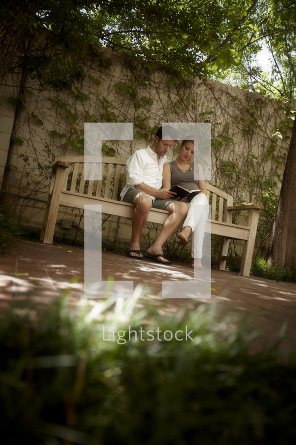 A young married couple sits on a bench reading God's word.