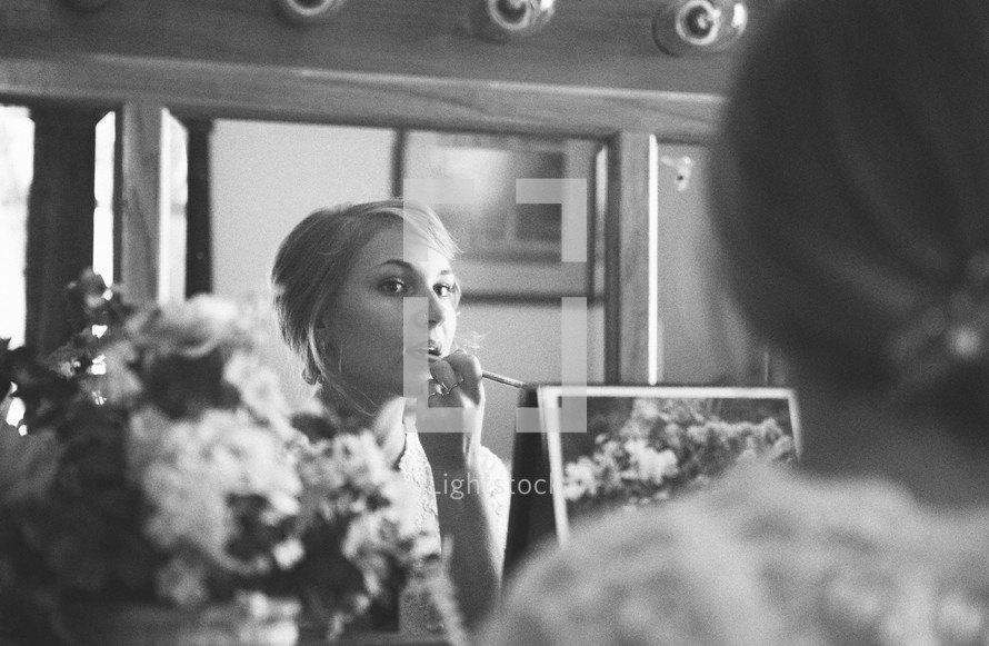 Woman looking in mirror applying lipstick