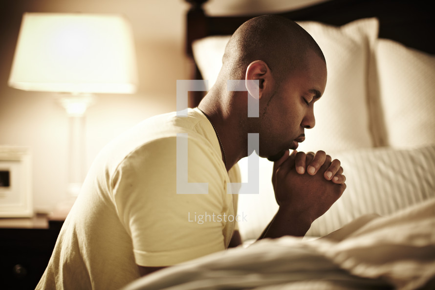 An African American man bowing in prayer before bedtime.