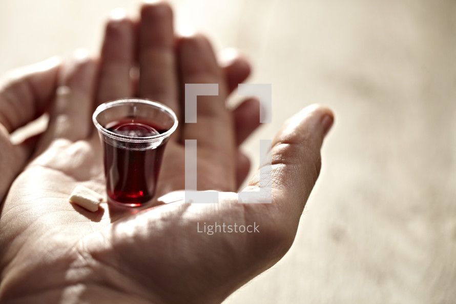 A communion cup and wafer in the palm of a hand