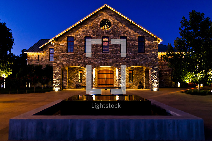 lighted stone building with wooden doors  sunset blue hour reflection fountain water night winery