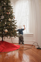 Boy hiding in the curtains behind the Christmas tree.