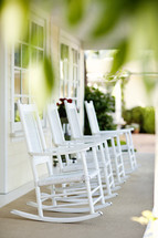 Four white rocking chairs sitting on front porch.