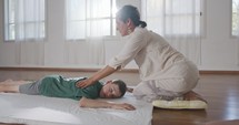 Shiatsu treatment. Masseuse giving treatment to a young boy, pressing on his back and neck