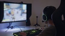 Young boy sitting in front of a computer, playing a game wearing a headset