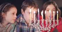 Three young kids watching Hanukkah candles burning.