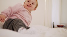 Cute baby girl sitting on a bed, playing, rolling and laughing