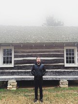man standing in front of a cabin in fog 