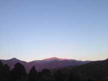 Silhouette of a treeline in front of a mountain range.