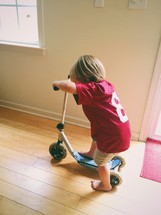 A small boy playing indoors on a small scooter.