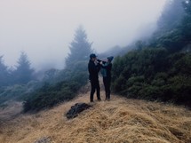 man and woman standing on a foggy mountain top 