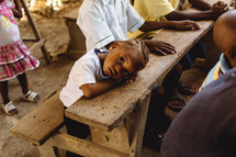 a child with his head on a desk in a classroom in Haiti 