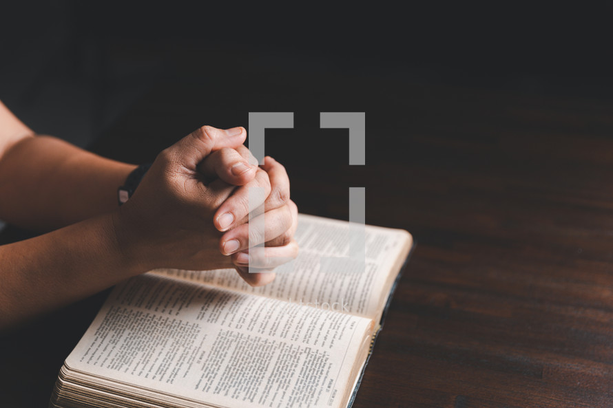 Hands clasped in prayer on Bible