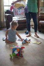 a mother with a laundry basket and her toddler playing on the floor 