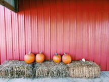 pumpkins on hay bales in front of a red barn 