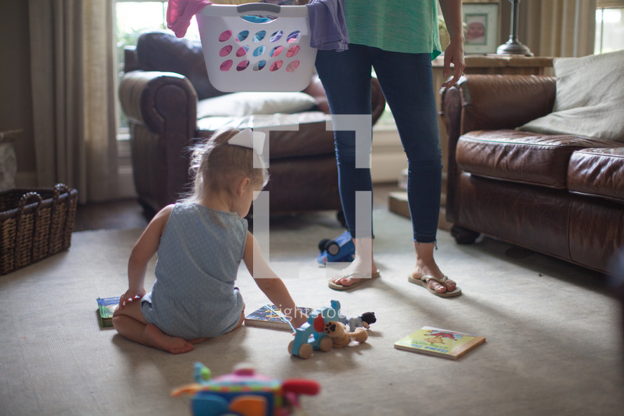 a mother holding a laundry basket and little girl playing with toys 