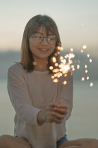 a young woman holding a sparkler on a beach 