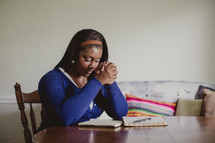 African-American woman praying and reading a Bible and a notebook