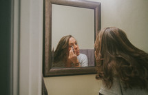 A young woman putting on makeup in the mirror 