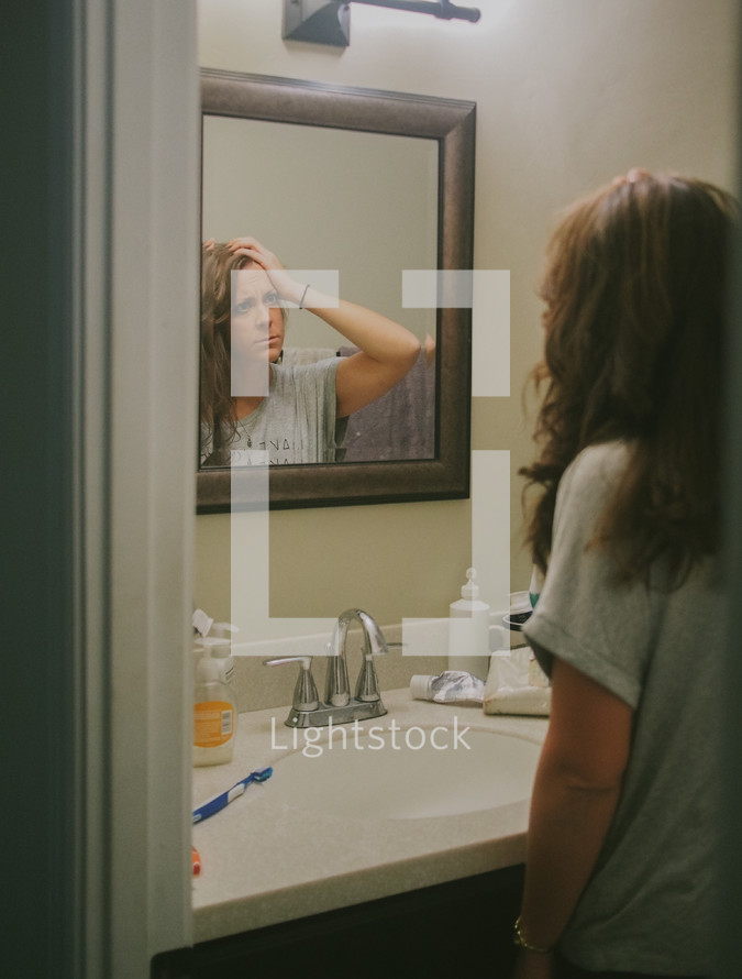 A young woman looking at herself in a mirror reflecting on her self image.