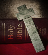 Dollar bill cross leaning against a Bible.