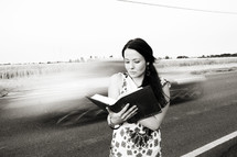 woman reading a Bible in front of speeding cars on a highway