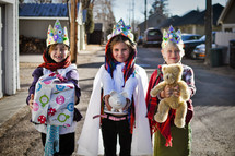 children dressed as the three kings a holding Christmas gift, teddy bear, and piggy bank 