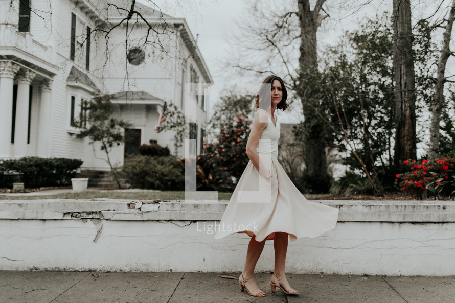 a woman in a dress walking down a neighborhood sidewalk 