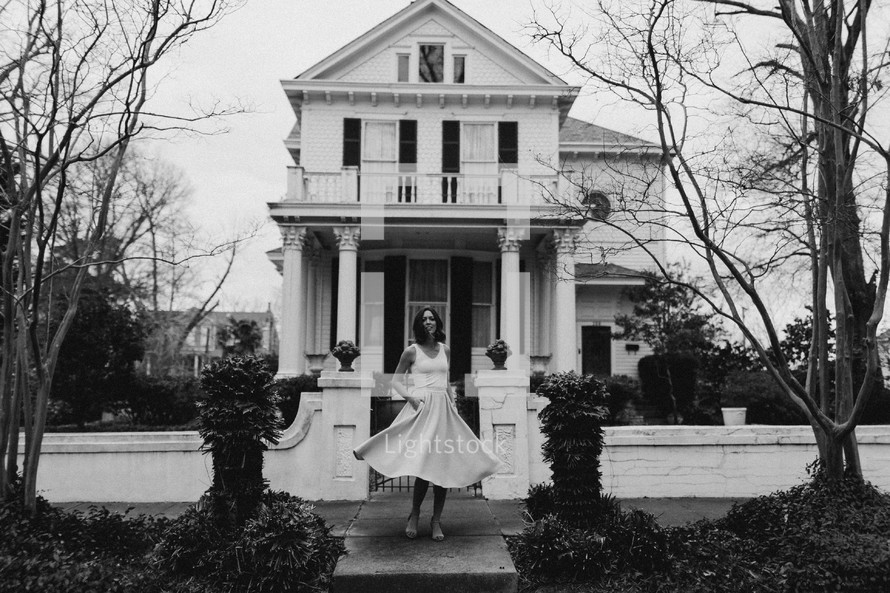 a woman in a dress twirling on a sidewalk in front of a house 
