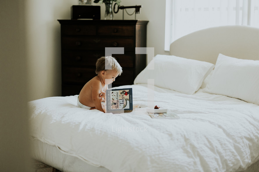 a toddler reading a book on a bed 