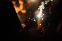 holding a sparkler by a campfire 