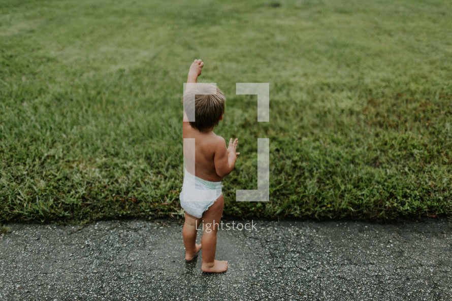 toddler boy in a diaper waving in the grass