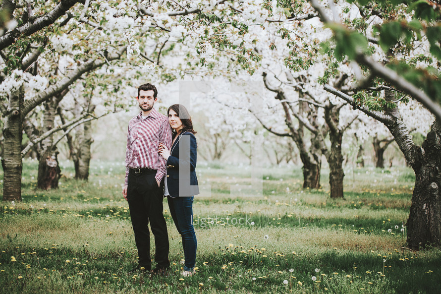 a couple standing in an orchard in spring 
