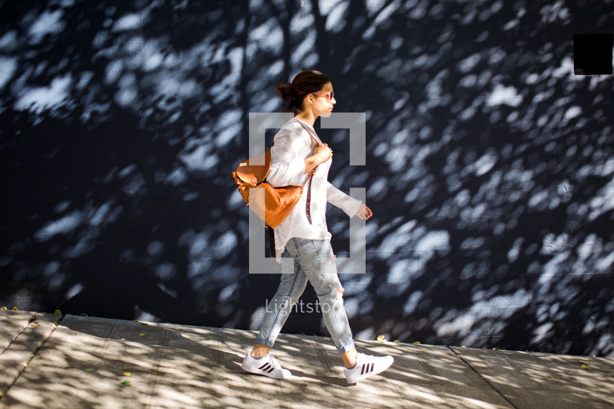 a woman walking on sidewalk carrying a backpack purse 