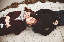 a couple lying on the sidewalk looking up at the camera 