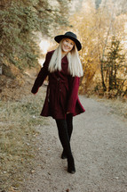 a young woman in a maroon coat and hat standing outdoors 